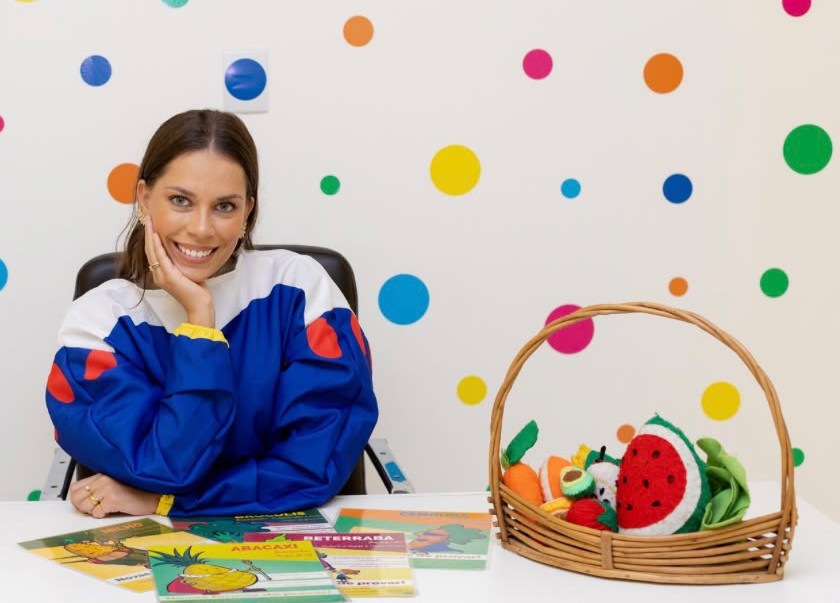 Rebeca Costa, nutricionista infantil, sorrindo em seu consultório colorido com materiais de nutrição para crianças
